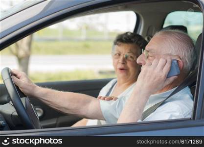 Elderly man on telephone while driving, wife in passenger seat