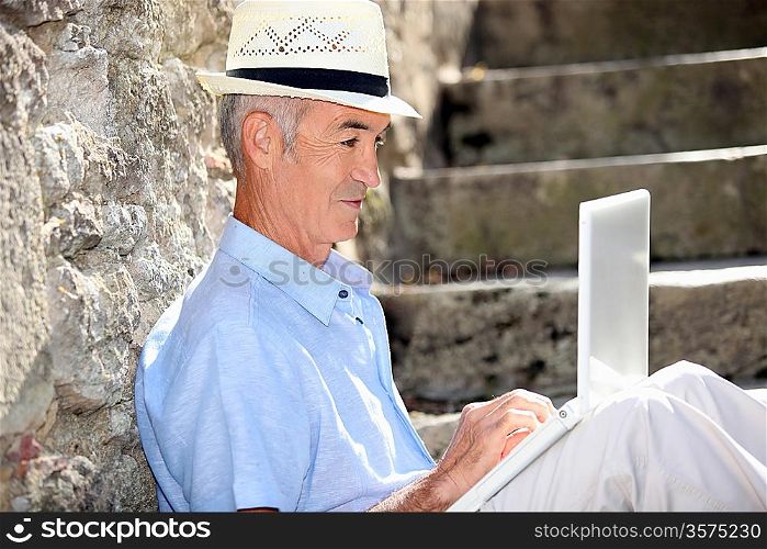 Elderly man sat on steps with laptop