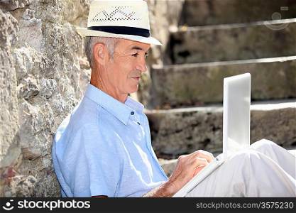 Elderly man sat on steps with laptop