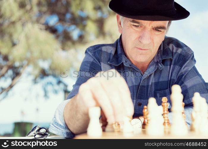 Elderly man sitting outdoors with chess. Thinking chess strategy