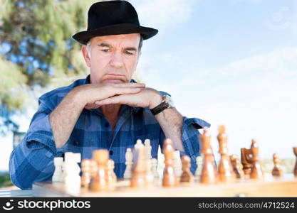 Elderly man sitting outdoors with chess. Thinking chess strategy