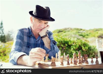 Elderly man sitting outdoors with chess. Thinking chess strategy