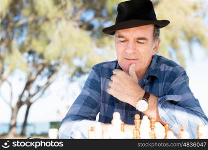 Elderly man sitting outdoors with chess. Thinking chess strategy