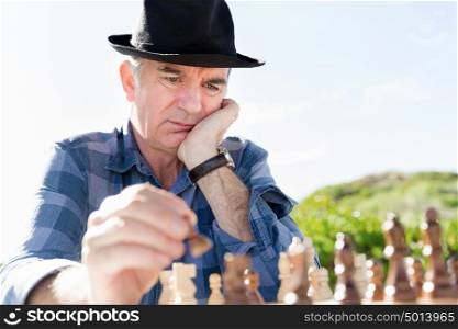 Elderly man sitting outdoors with chess. Thinking chess strategy