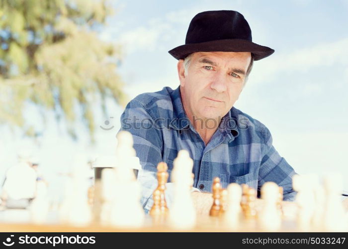 Elderly man sitting outdoors with chess. Thinking chess strategy