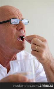 Elderly man swallowing a pill