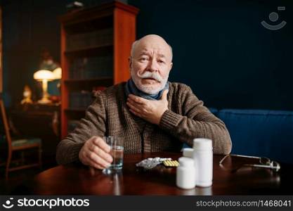 Elderly man takes pills in home office, age-related diseases. Mature senior is ill and being treated in his house. Elderly man takes pills in home offic