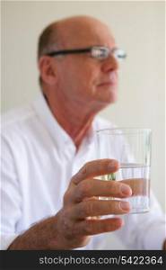 Elderly man taking medication with glass of water
