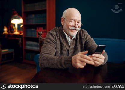 Elderly man using mobile phone in home office. Bearded mature senior with smartphone in living room, old age businessman. Elderly man using mobile phone in home office