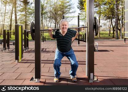 Elderly man warming up at the weights bar in the fitness park (outdoors gym). Warming up in the fitness park