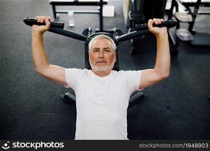 Elderly man, workout on exercise machine, gym interior on background. Sportive grandpa on fitness training in sport center. Healty lifestyle, health care, old sportsman. Elderly man, workout on exercise machine, gym