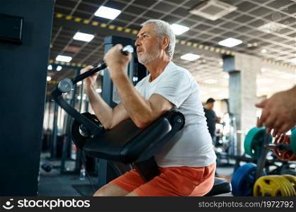 Elderly man, workout on exercise machine, gym interior on background. Sportive grandpa on fitness training in sport center. Healty lifestyle, health care, old sportsman. Elderly man, workout on exercise machine in gym