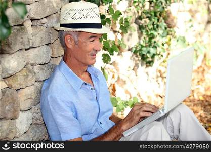 Elderly map sat against wall with laptop