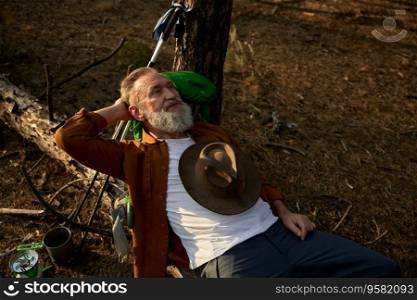 Elderly retired man hiker rest on log surrounded pine forest environment. Happy relaxed male traveler taking break enjoying beautiful natural environment during weekend trip recreation. Elderly man hiker rest on log surrounded pine forest environment