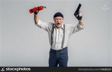 Elderly robber poses with dynamite and gun on grey background, gangster. Mature senior in studio, man in old age. Elderly robber poses with dynamite and gun