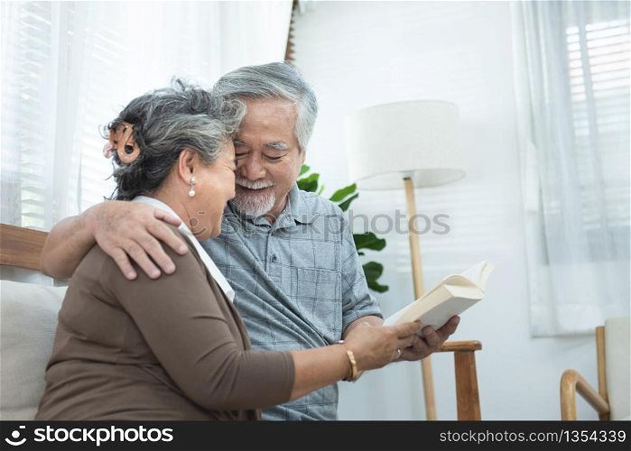 Elderly senior asian couple sitting on sofa reading book together at home.Retirement grandmother and grandfather spend time together at house.
