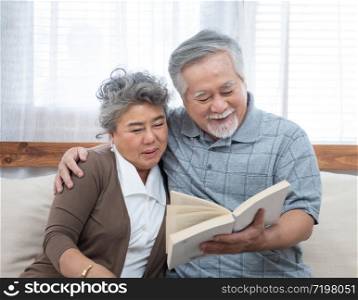 Elderly senior asian couple sitting on sofa reading book together at home.Retirement grandmother and grandfather spend time together at house.