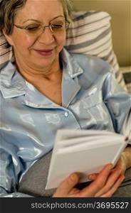 Elderly smiling woman reading book lying in bed