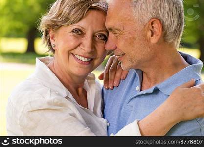Elderly wife and husband cuddling and smiling outdoors