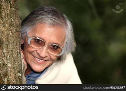 Elderly woman behind tree trunk