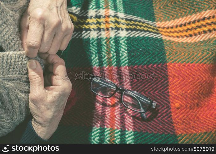 Elderly woman buttoning his vest. Glasses on blanket