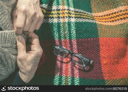 Elderly woman buttoning his vest. Glasses on blanket