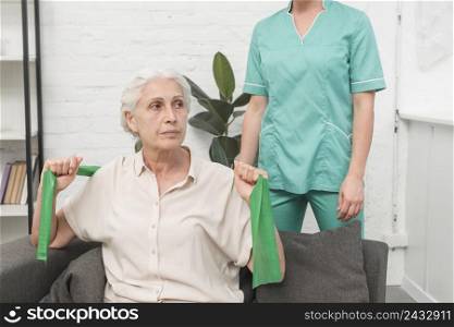 elderly woman exercising with green stretch band sitting front female nurse