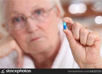 Elderly woman holding a capsule between her fingers