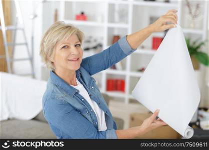 elderly woman holding paper roller for wallpaper redecoration