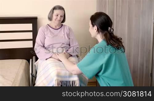 Elderly woman on wheelchair talking with her care assistant. Nursing and caregiving at home or hospice concept. Slow motion