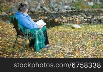 Elderly woman reading a book outdoors Side View