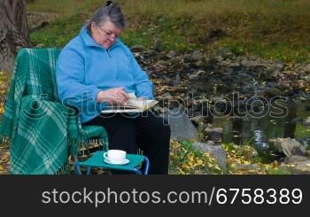 Elderly woman reading a book with a cup of coffee in the park.