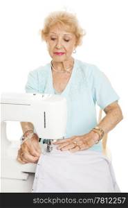 Elderly woman sews with her sewing machine. Isolated on white.
