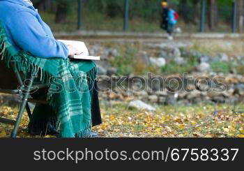 elderly woman sitting in a chair at autumn park reading book, Unrecognisable Person, Side View