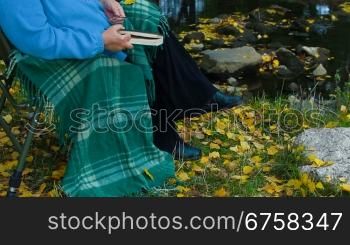 elderly woman sitting in a chair at autumn park reading book, Unrecognisable Person, Side View