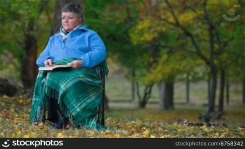 elderly woman sitting in chair sheltered blanket and reading book, Front View