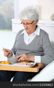 Elderly woman sitting in sofa with lunch tray