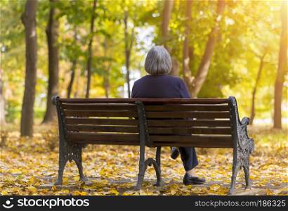 Elderly woman sitting on a bench in autumn park. Lonely aged woman sitting on bench in autumn park lookes at trees.