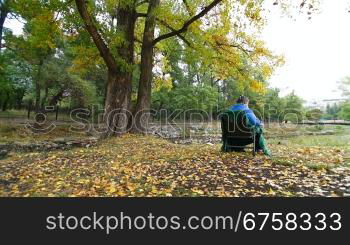 elderly woman sitting on a chair at autumn park. Tripod, Wide Shot, Rear View