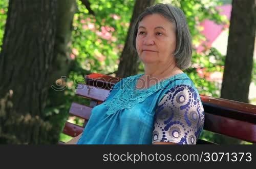 Elderly woman sitting on park bench thinking.