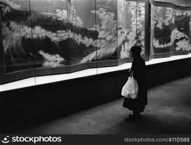 Elderly woman stands looking at shop window