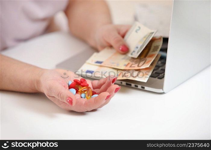 Elderly woman with laptop holding money, euro cash and pills on white table, copy space. Concept of treatment cost, medicine price, health insurance budget.. Elderly woman with laptop holding money, euro cash and pills on white table, copy space. Concept of treatment cost, medicine price, health insurance budget