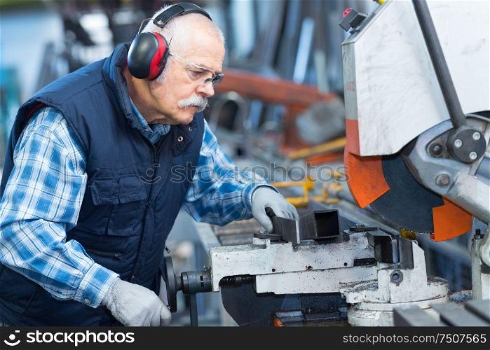 elderly worker watches processing of detail on milling machine