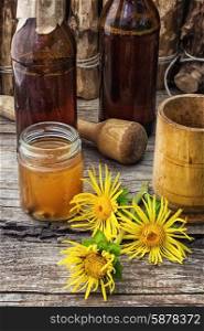 Elecampane tincture. infusion of inflorescences and roots of the medicinal plant Inula on the wooden table next mortar and pestle.Photo tinted.Selective focus