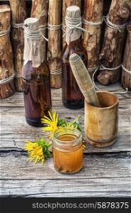 Elecampane tincture. infusion of inflorescences and roots of the medicinal plant Inula on the wooden table next mortar and pestle.Photo tinted.