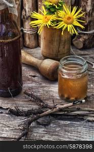 Elecampane tincture. infusion of inflorescences and roots of the medicinal plant Inula on the wooden table next mortar and pestle.Photo tinted.
