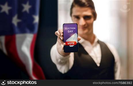 Election Day in United States Concept. Young Man presenting Online Vote on Mobile Phone Screen. USA Flag as background