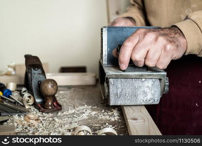 Electric belt sander, male hand sander. Workpiece processing on light brown wooden table. front view