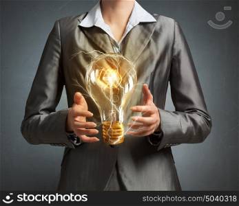 Electric bulb in woman hand. Close up of businesswoman holding glass glowing light bulb in hands