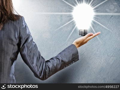 Electric bulb. Rear view of businesswoman holding bulb in palm